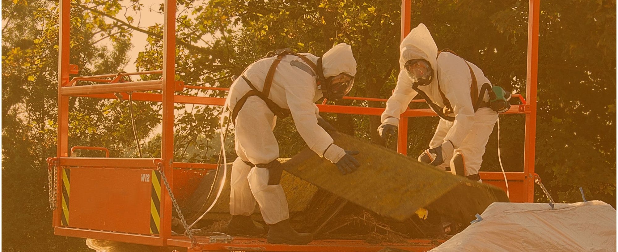 Two people in asbestos protective equipment throw asbestos away
